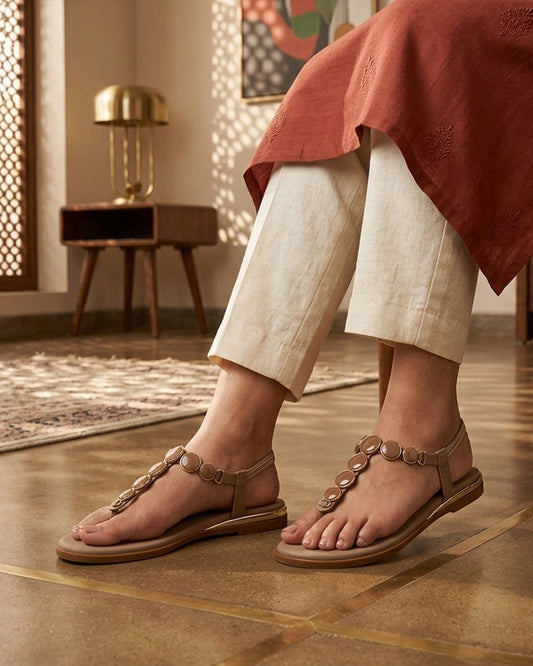 Women's beige T-strap thong flat sandals with metallic disc strap and back strap, on-foot view